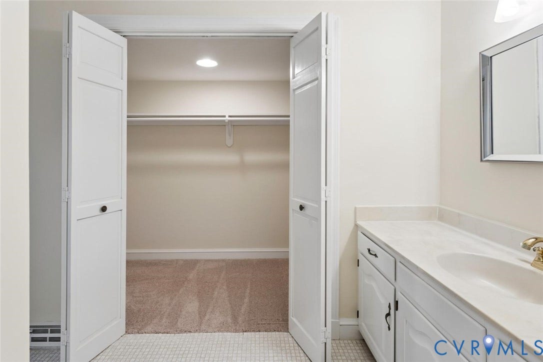 White bi-fold closet doors, recessed lighting, wall-mounted mirror, white vanity with integrated sink, and brass-tone faucet