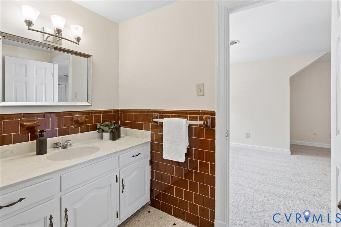 White vanity with integrated sink, brown tiled backsplash, wall-mounted mirror, and overhead light fixture