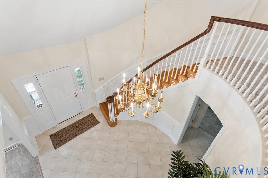 Foyer featuring a grand chandelier, curved staircase with wood-finish steps, and a white paneled entry door with sidelights