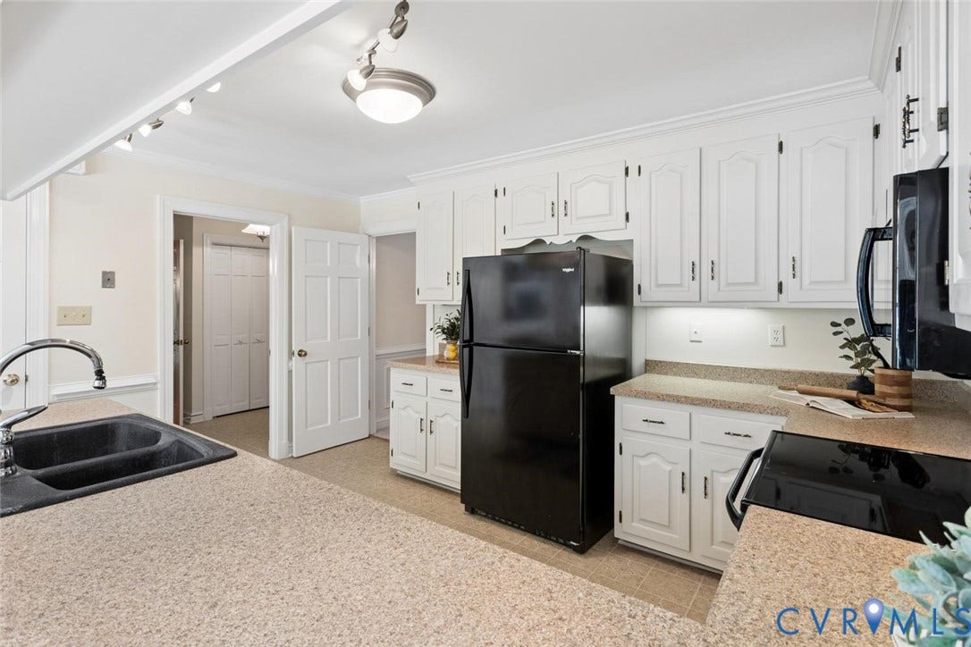 White cabinetry with dark hardware, speckled countertops, and a black double basin sink