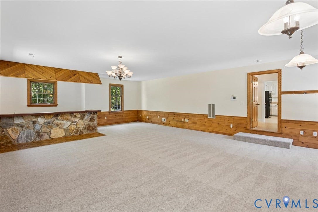 Spacious room featuring carpeting, wood paneling, a stone-faced bar, and multiple windows