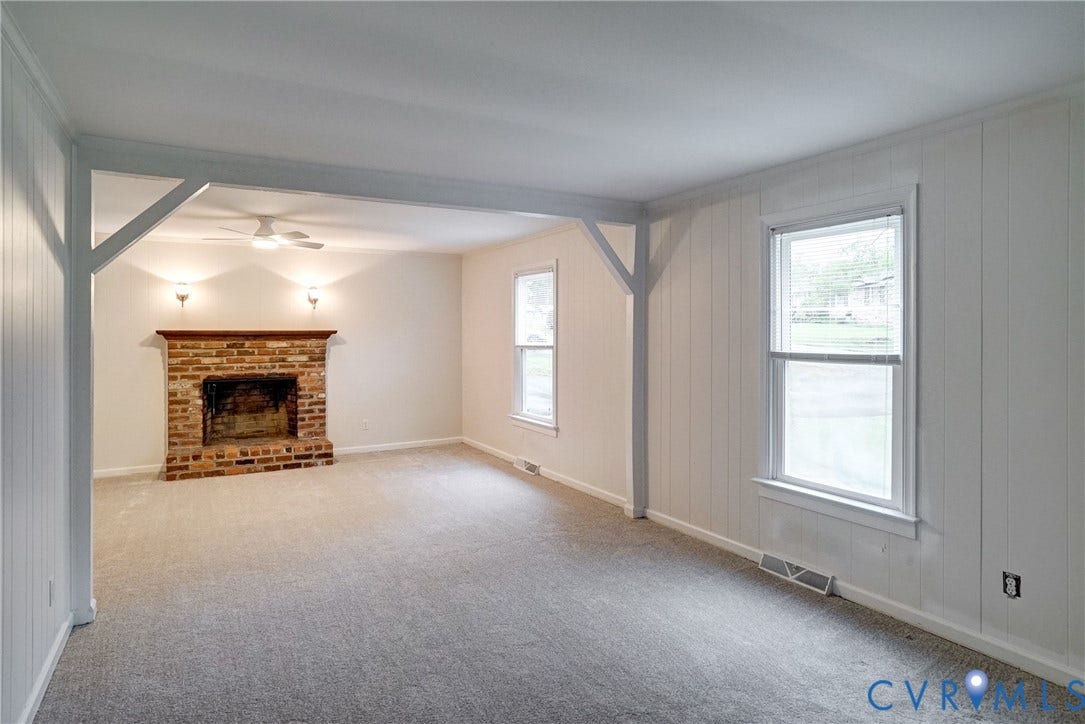 2602 Seacliff Court, Richmond, VA 23236 Spacious room featuring a brick fireplace with a wood mantle, neutral carpet flooring, white paneled walls, and two double-hung windows