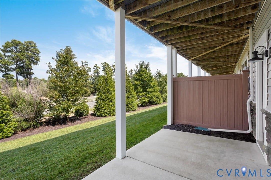 10420 Perennial Drive, Ridgefield Green Townhome, Henrico, VA 23233 Expansive concrete patio, manicured lawn, brown privacy screen, exterior wall sconce, and mature trees