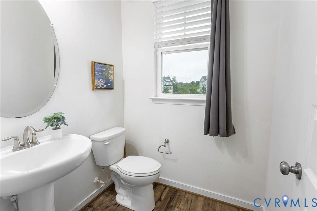 10420 Perennial Drive, Ridgefield Green Townhome, Henrico, VA 23233 Pedestal sink with brushed nickel faucet, oval mirror, window with blinds, and wood-finish flooring