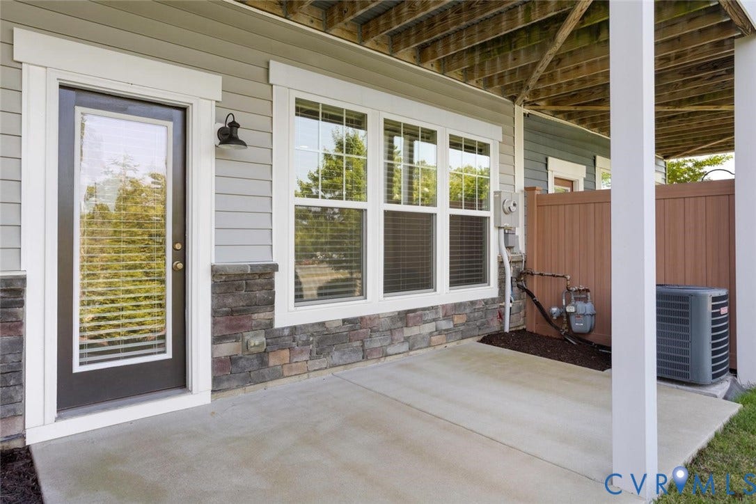 10420 Perennial Drive, Ridgefield Green Townhome, Henrico, VA 23233 Concrete patio featuring a full-light exterior door, multiple windows, stone veneer accents, and vinyl siding