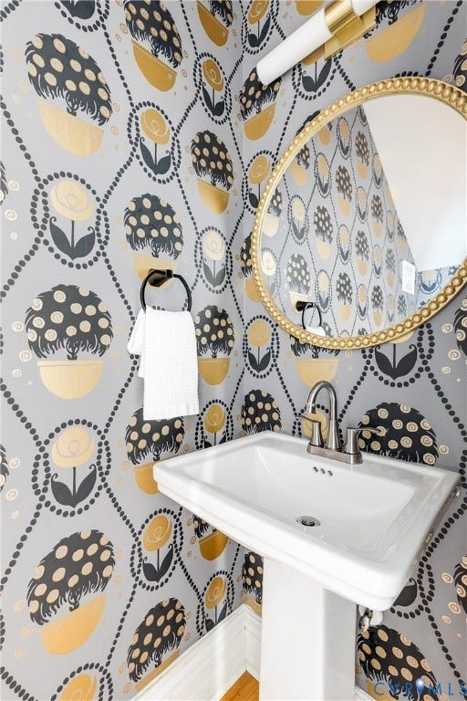 1416 Oakwood Avenue, Church Hill, Richmond, VA 23223 Half bathroom. Pedestal sink with polished chrome faucet, framed by a gold-accented oval mirror and decorative wall covering