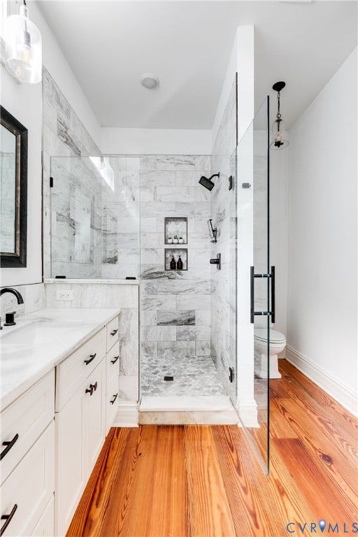 1416 Oakwood Avenue, Church Hill, Richmond, VA 23223 Hardwood flooring, white vanity with stone countertop, glass-enclosed shower with tiled walls, dual shower heads, and built-in shower niches