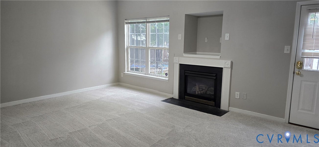 5506 Millwheel Lane, Henrico, VA 23228 Living area featuring light grey wall paint, grey carpet, a white framed window, and a built-in fireplace with a white mantle and black surround