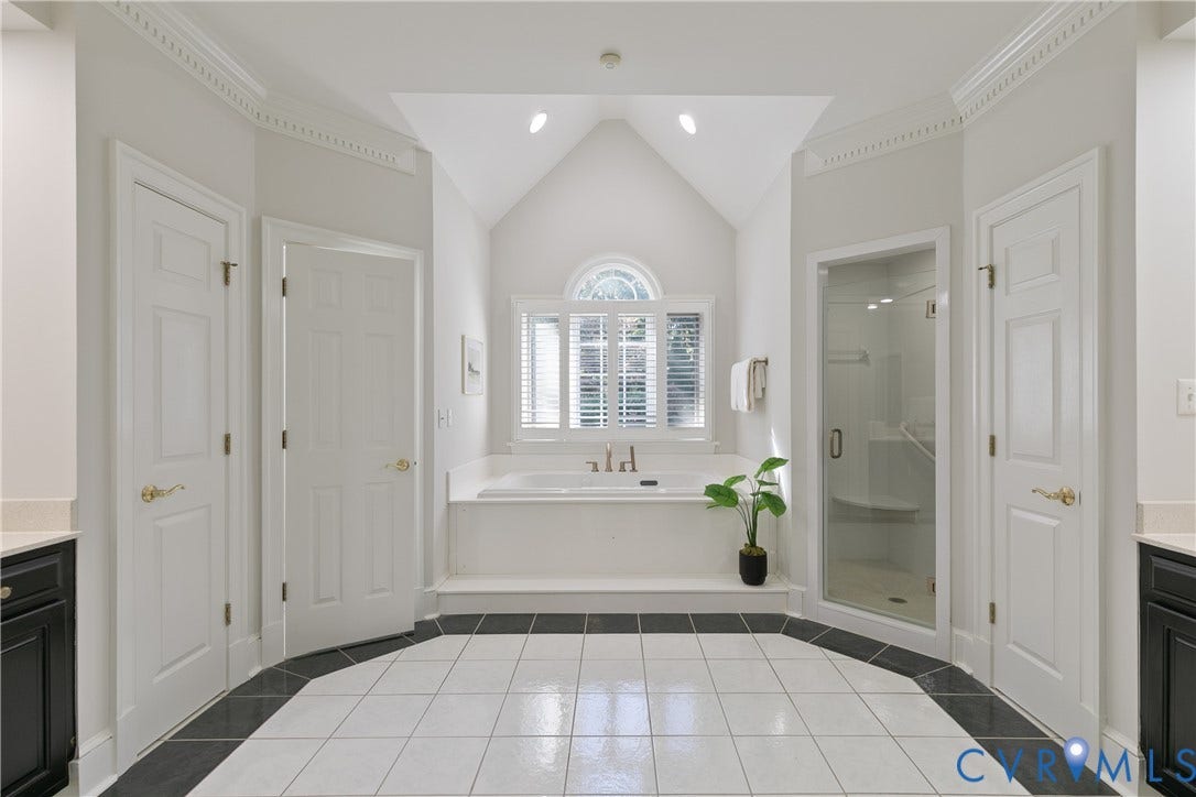 2621 Glenalmond Court, Powhatan, VA 23139 Expansive bathroom featuring a vaulted ceiling with recessed lighting, a built-in soaking tub, a glass-enclosed shower, dual vanities with dark cabinetry, and white tile flooring with a dark border