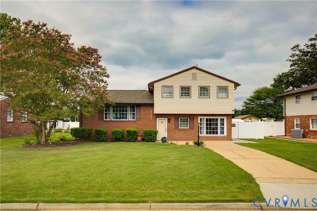 Brick and siding exterior, expansive front lawn, mature tree, concrete driveway, and white picket fencing