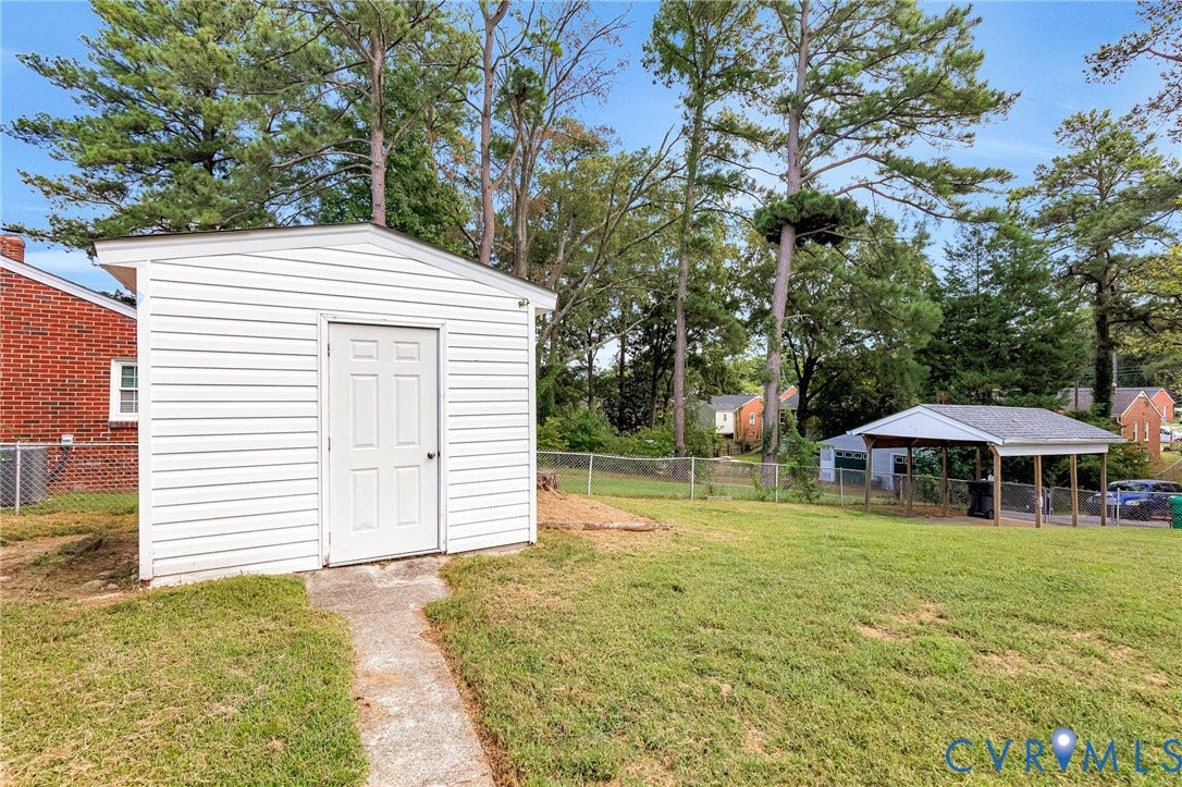 507 Walnut Avenue, Walnut Court, Colonial Heights, VA 23834 Expansive backyard featuring a white storage shed with a panel door, a covered carport structure, chain-link fencing, and mature trees