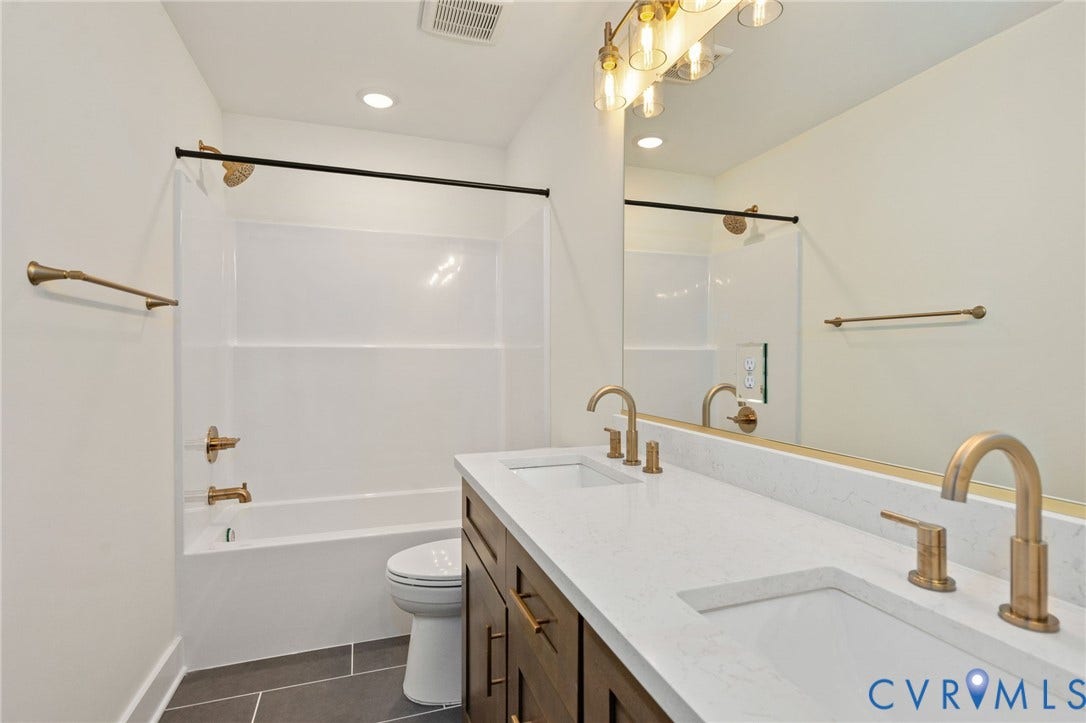 7603 Oster Drive, Chamberlayne Farms Area, Henrico, VA 23227 Dual vanity with undermount sinks and light-toned countertops, warm-toned cabinet finishes, brushed gold fixtures, overhead vanity lighting, and a combination tub and shower