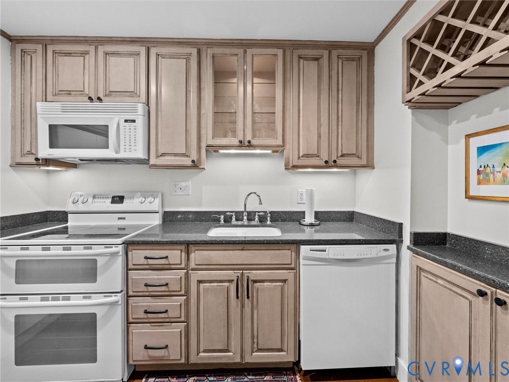 Kitchen featuring light wood-finish cabinetry, dark countertops, a double oven, a built-in microwave, and a built-in wine rack