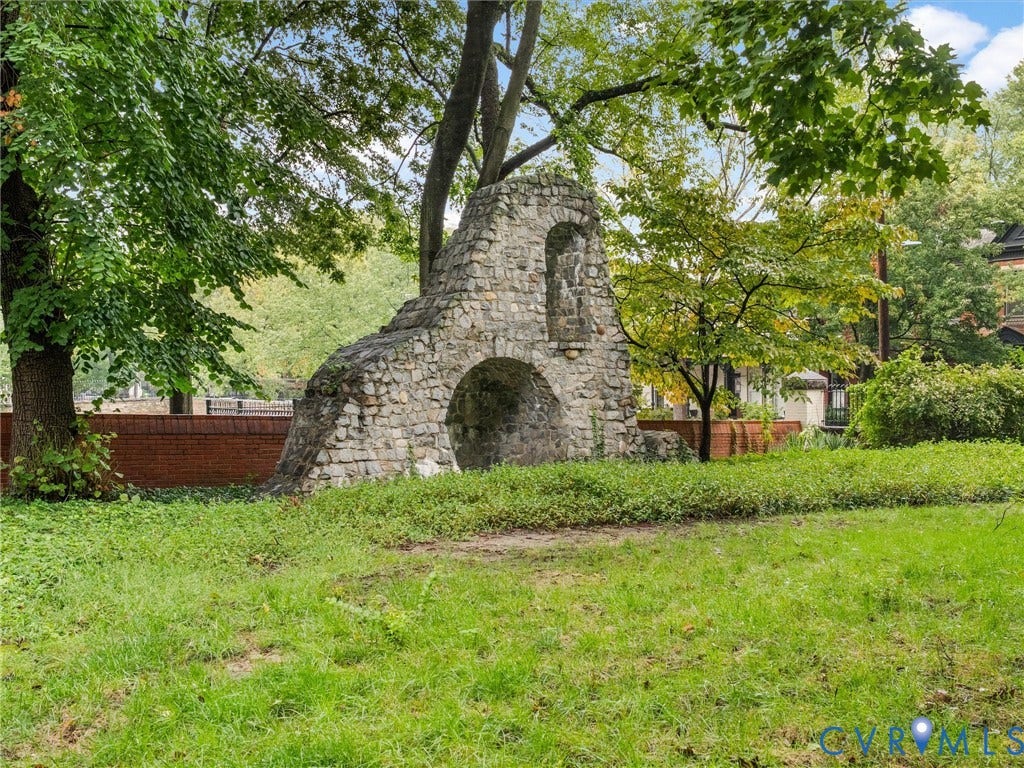 Stone architectural feature with an arched opening, surrounded by mature trees and a manicured lawn