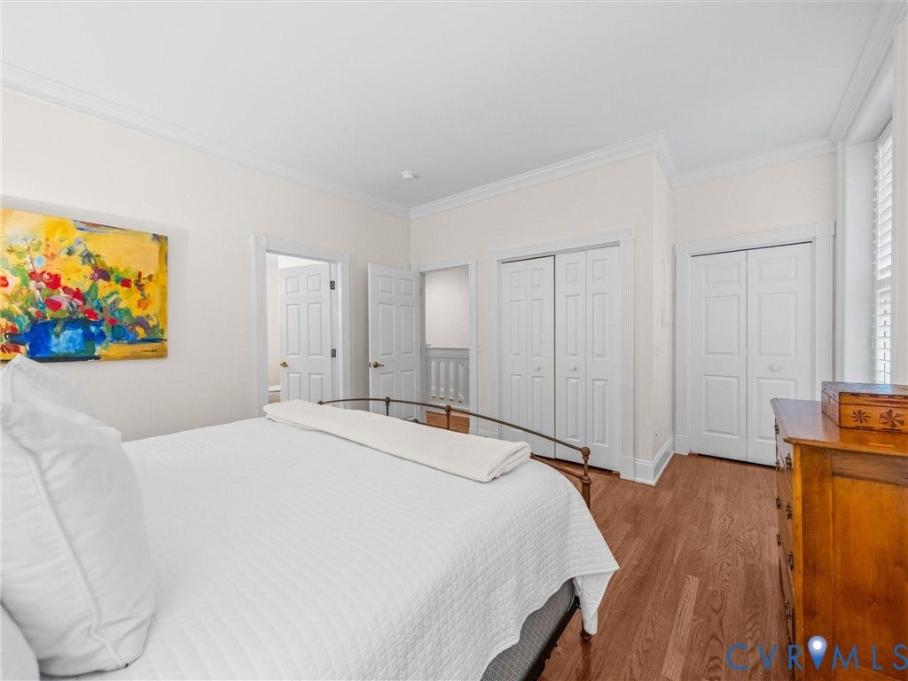 Wood-finish flooring, crown molding, white paneled doors, and louvered window treatments