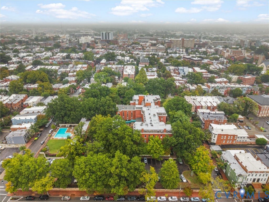 Aerial perspective featuring a residential urban landscape with mature trees, a swimming pool, and dedicated parking areas