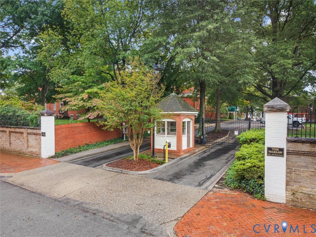 Gated community entrance featuring a guardhouse, brick walls, and mature trees