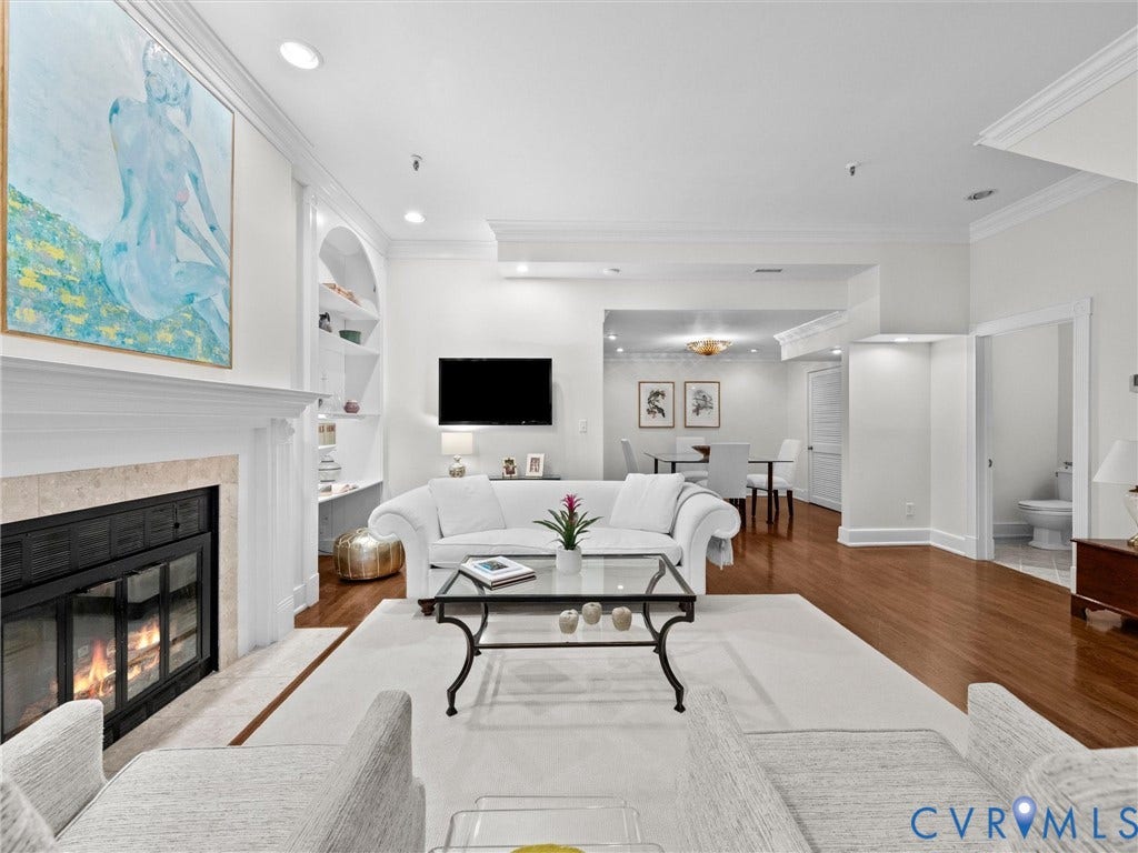 Fireplace with stone surround, custom built-in shelving, wood-finish flooring, recessed lighting, and crown molding