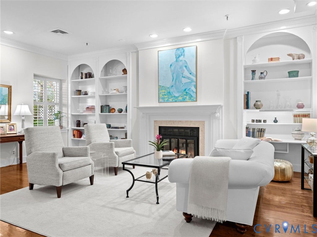 Fireplace with an ornate mantel, built-in arched shelving, shuttered window, recessed lighting, and wood-finish flooring