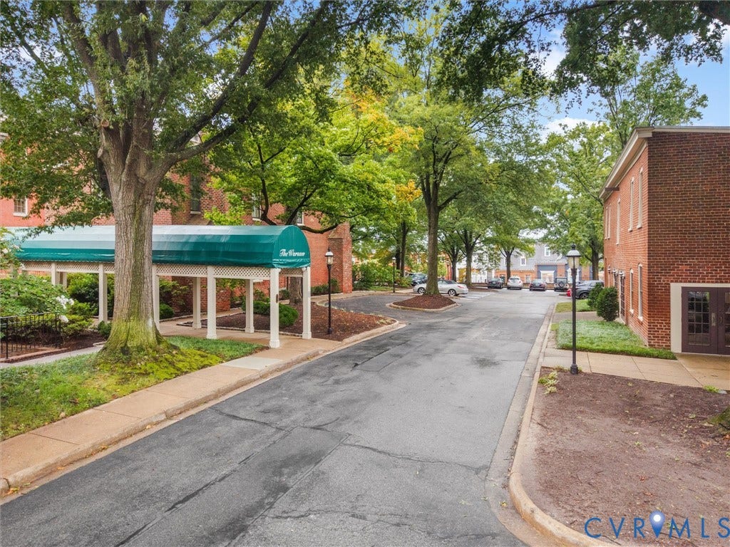 Brick exterior building with a green awning entrance, mature trees, and paved parking areas