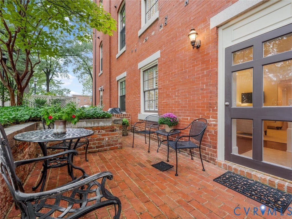 Brick exterior with a brick patio, featuring a glass-paneled entry door, an exterior wall sconce, and a raised planting bed