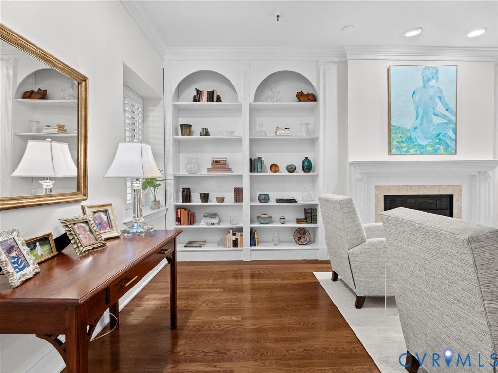 Hardwood flooring, recessed lighting, built-in shelving with arched tops, a decorative fireplace with a stone surround, and white plantation shutters