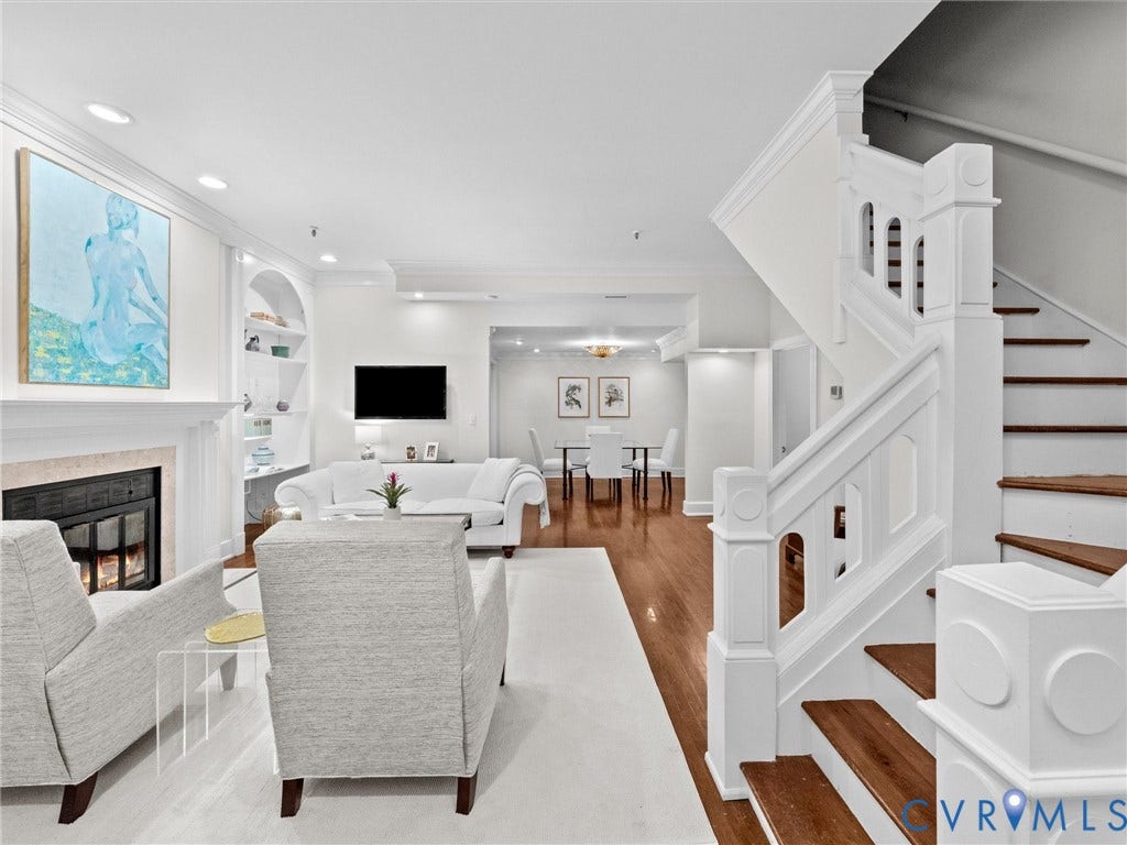 Hardwood flooring throughout, a traditional fireplace with a stone surround, and an intricate white staircase with wood treads