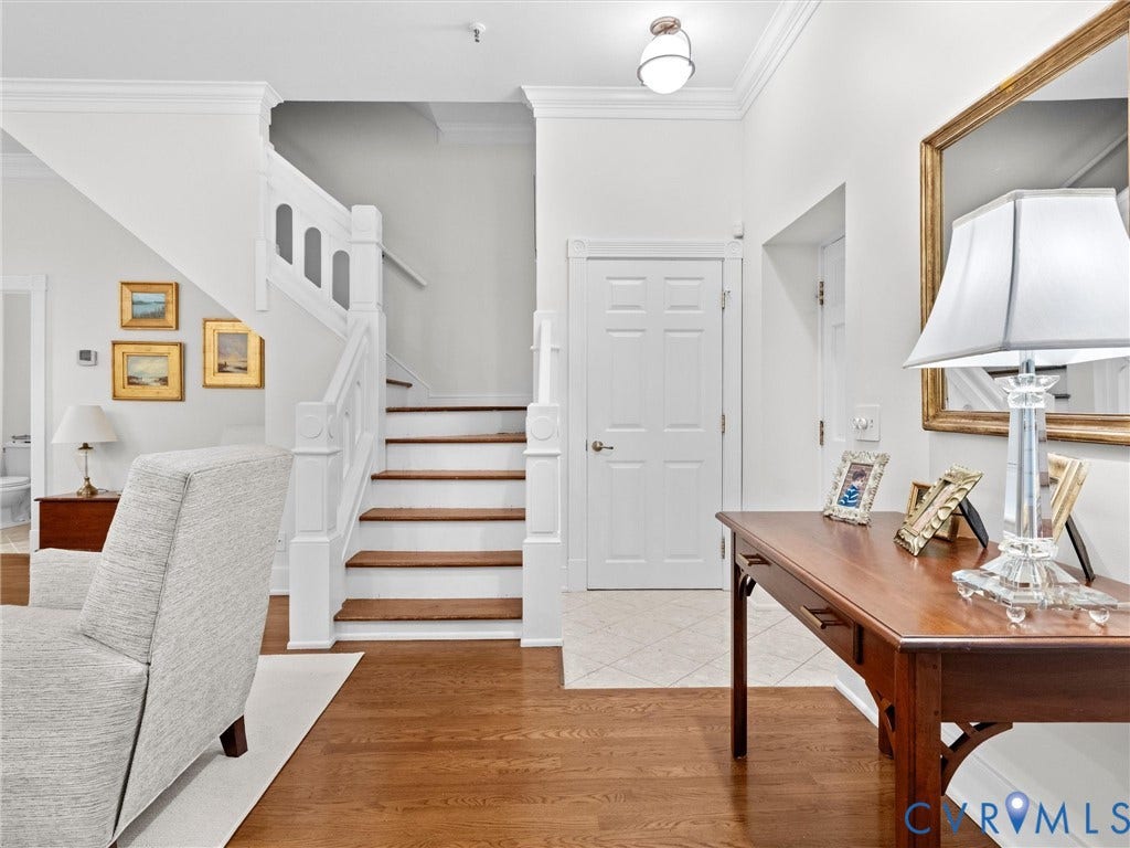 Hardwood flooring, painted white staircase with wood treads, crown molding, paneled interior door, and a flush mount ceiling light fixture