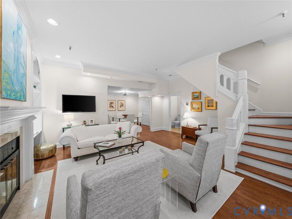 Living area featuring hardwood flooring, a fireplace with a stone surround, recessed lighting, and a staircase with a white banister