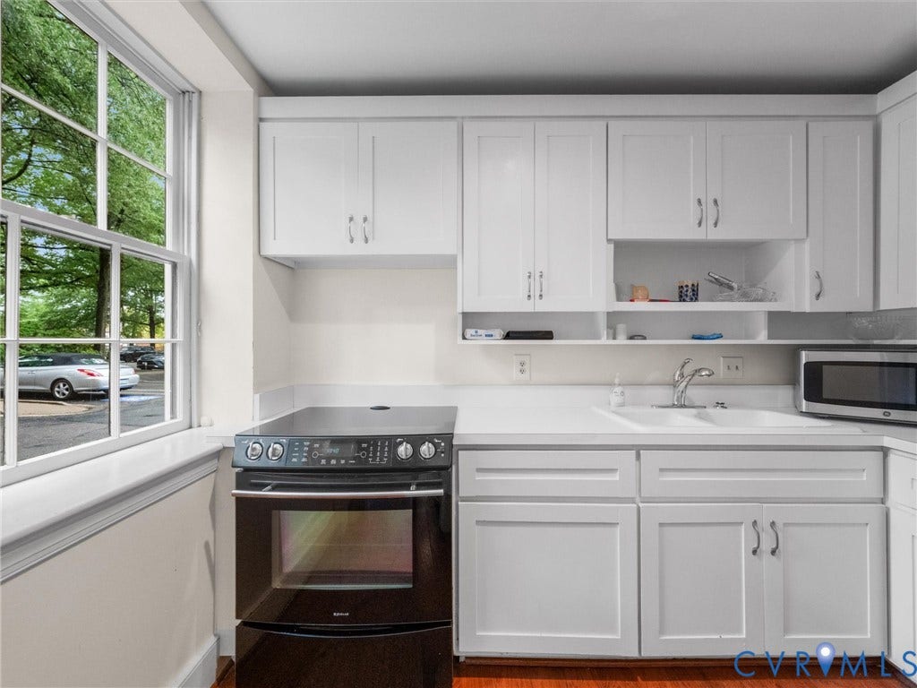 White shaker-style cabinetry, white countertops, built-in dual basin sink, black electric range, and wood-finish flooring