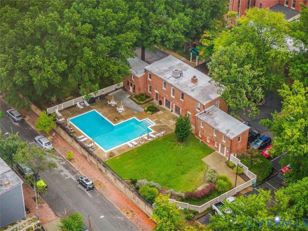 Brick exterior, outdoor swimming pool, manicured lawn, surrounding mature trees, and paved parking area