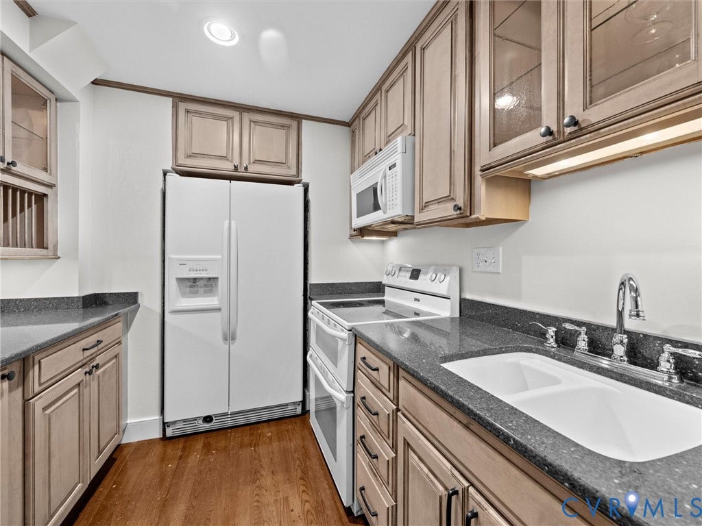Kitchen featuring wood-finish cabinetry, dark speckled countertops, wood-finish flooring, and a double basin sink with a chrome faucet