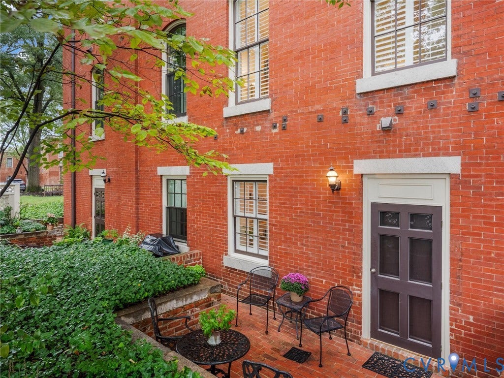 Brick exterior featuring multiple windows with white trim, a patio area with a brick surface, and an exterior wall lantern