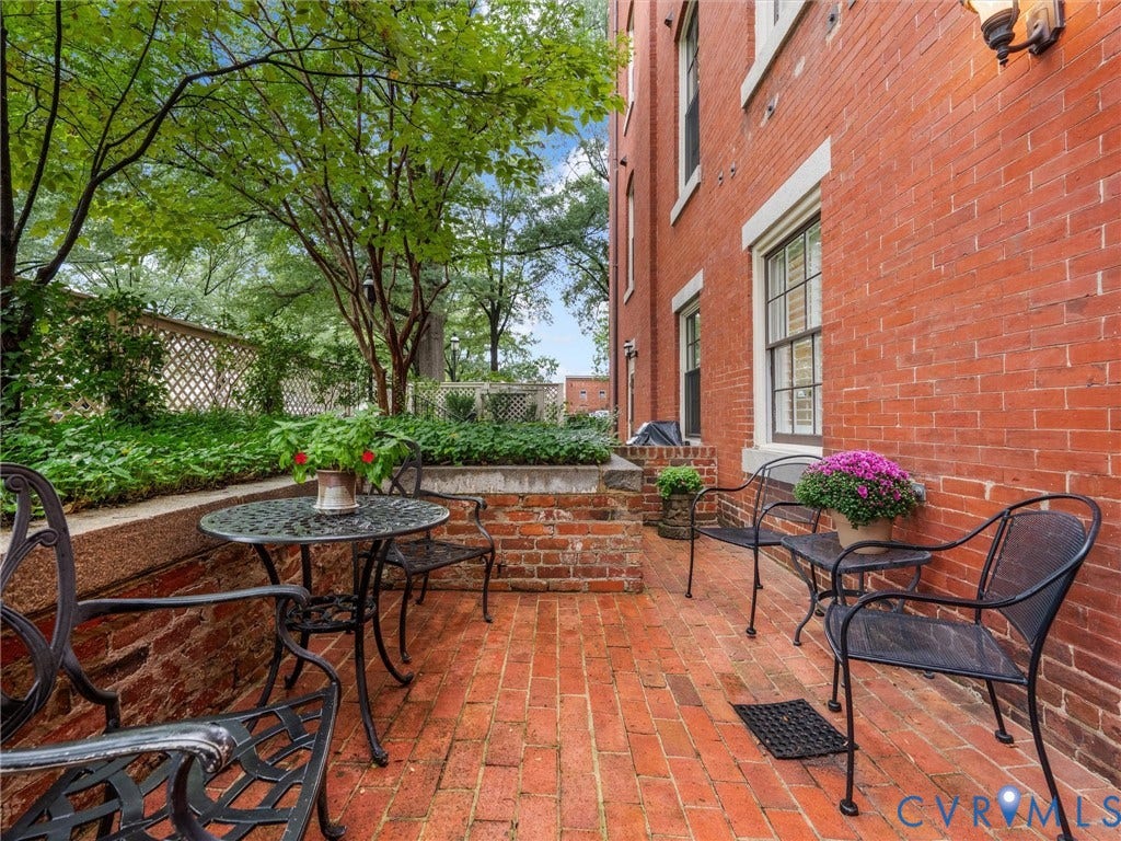 Brick exterior featuring multiple windows, a wall-mounted light fixture, and a brick patio