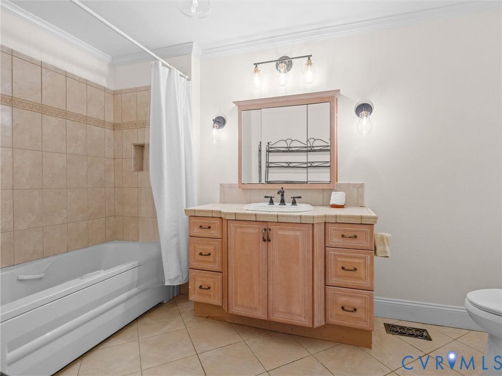 Vanity with integrated sink, tiled flooring, wood-finish cabinetry, and a bathtub with tiled surround