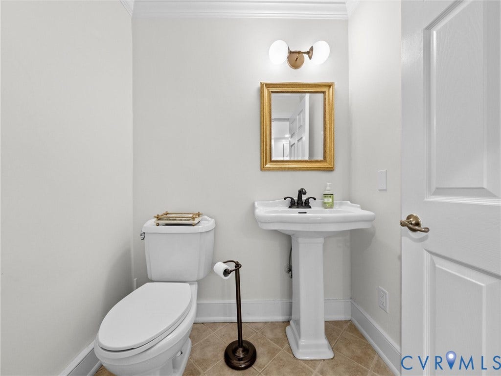 Pedestal sink with dark-toned fixtures, tiled flooring, and a gold-framed mirror