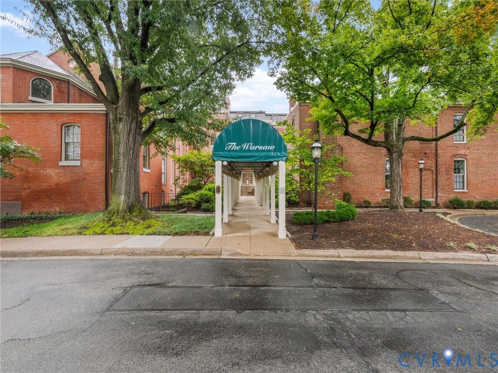 Brick building exterior with an arched window, a covered walkway featuring a green awning, and mature trees