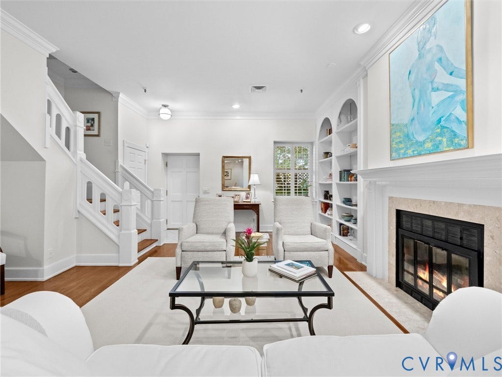 Wood-finish flooring, staircase with white newel posts, built-in shelving, stone-surround fireplace, and crown molding