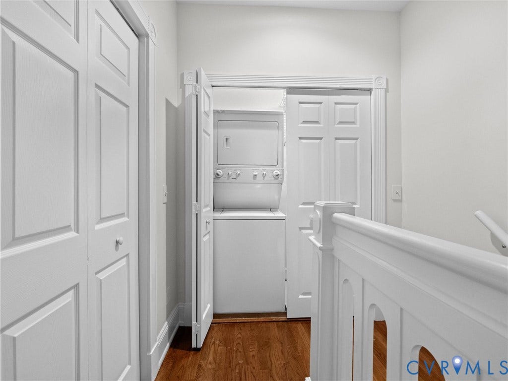Hardwood-finish flooring, white stackable washer and dryer, white paneled doors, and white painted balustrade