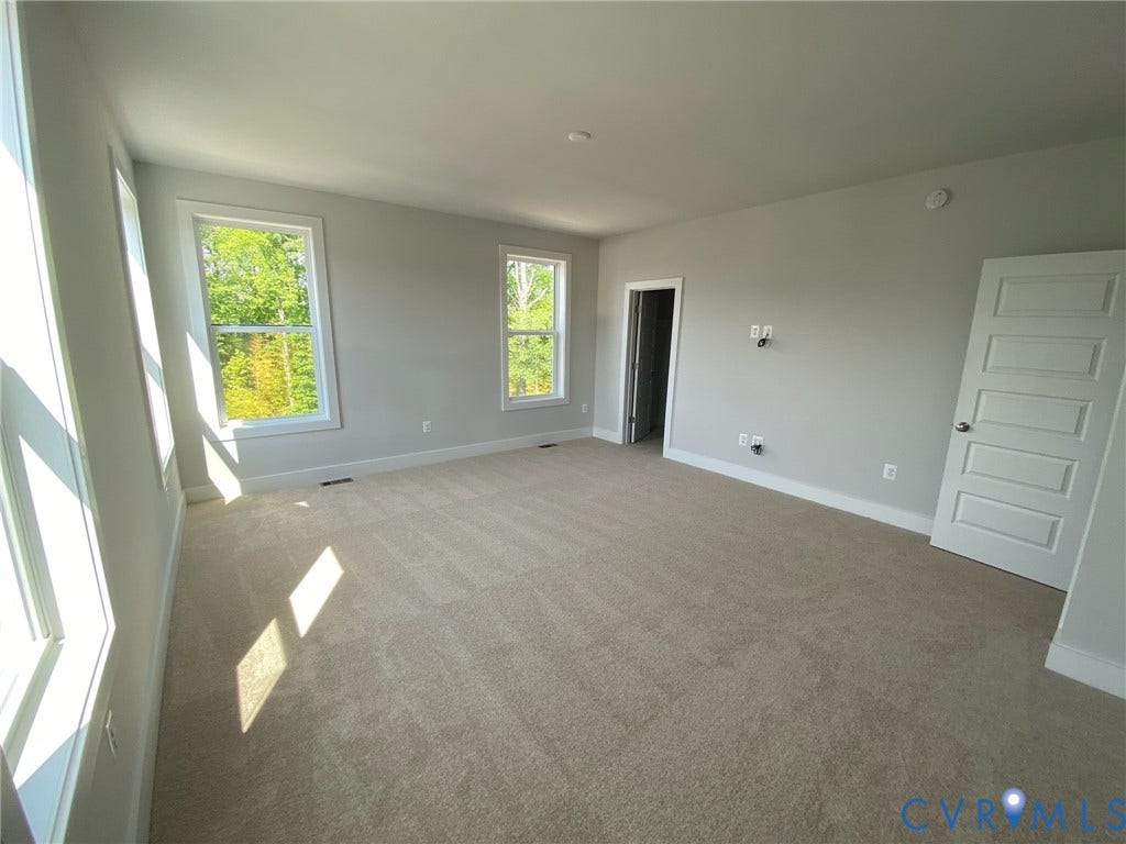 2701 St Elias Drive, #B, Richmond, VA 23294 Spacious room featuring neutral carpeting, light-toned wall paint, multiple windows, and a five-panel interior door