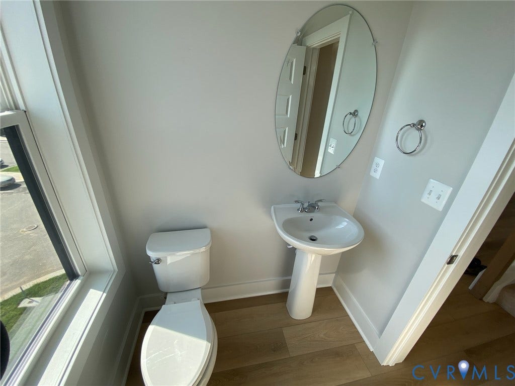 2701 St Elias Drive, #B, Richmond, VA 23294 Pedestal sink with chrome faucet, oval frameless mirror, and wood-finish flooring