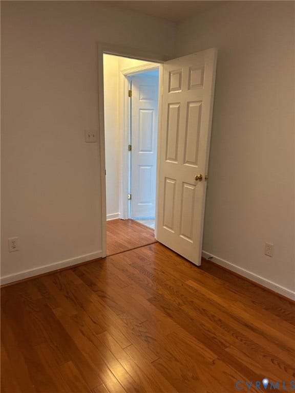 Hardwood flooring with a warm finish, white trim, and a white paneled door