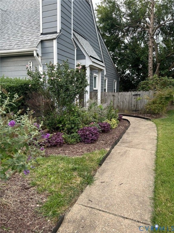 Gray siding exterior with white trim, a concrete walkway, established landscaping, and a wood privacy fence