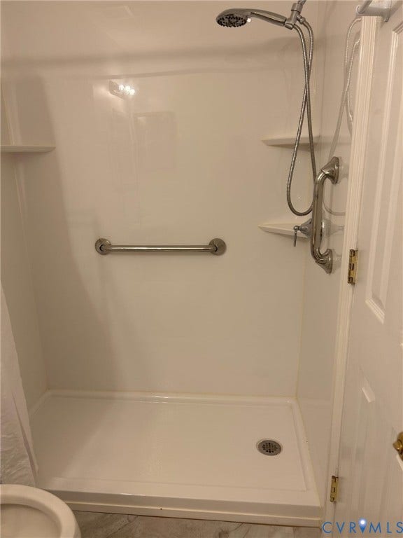 White shower enclosure with integrated shelving, handheld shower fixture, and grab bars