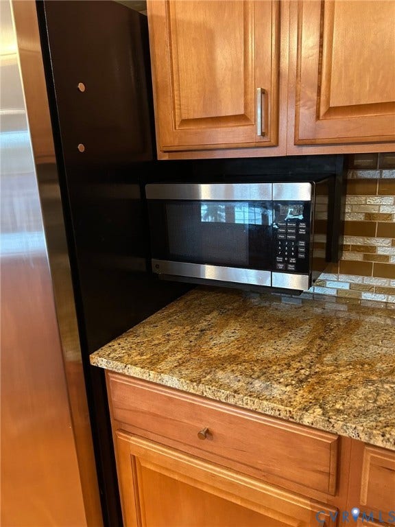 Granite-finish countertop, wood cabinetry, stainless steel microwave, and tile backsplash