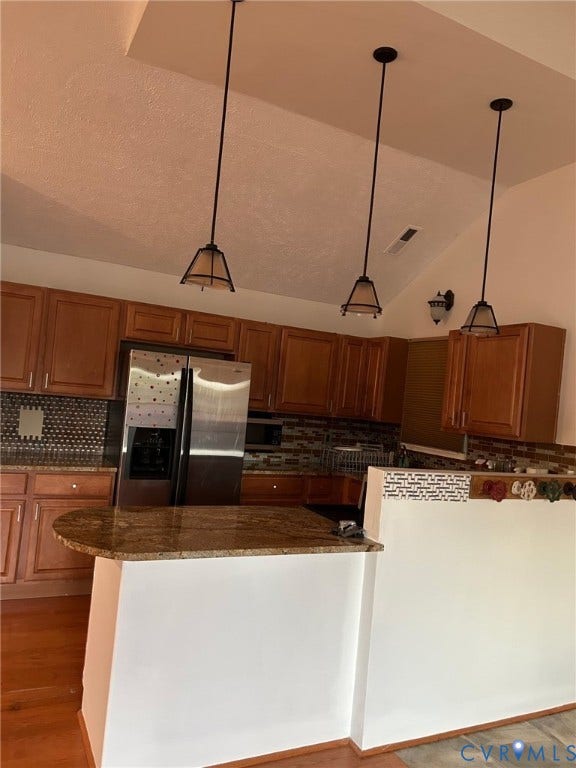 Vaulted ceiling, recessed lighting, wood-finish cabinetry, stone countertop island, stainless steel refrigerator