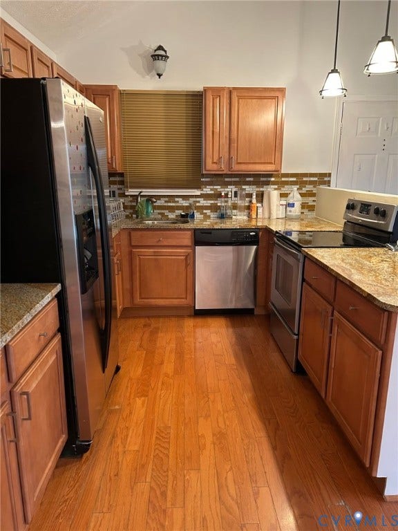 Kitchen featuring wood-finish flooring, stainless steel appliances, granite-style countertops, and a mosaic tile backsplash
