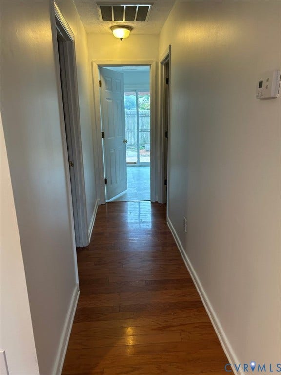 Wood-finish flooring throughout the hallway, leading to a door with outdoor access