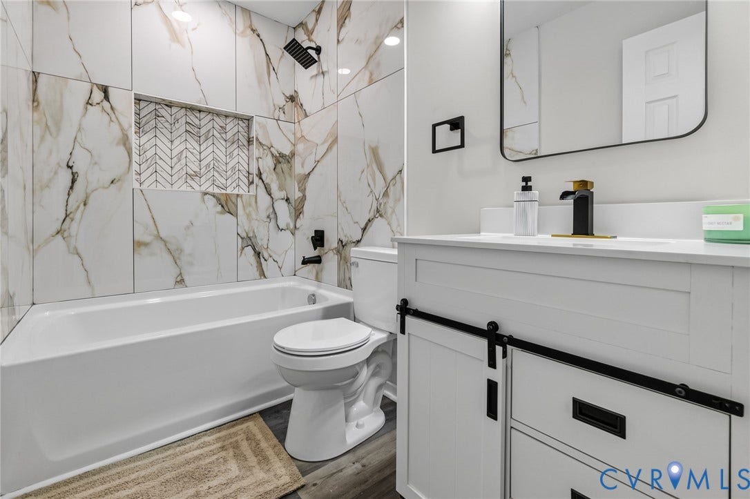 1146 Willcox Street, Petersburg, VA 23803 Contemporary bathroom featuring a white soaking tub with a black shower fixture, large format marbled wall tiles, a herringbone-patterned tile niche, a white vanity with barn door hardware, and a gold and black faucet