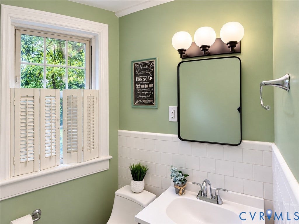 518 Central Terrace, Hopewell, VA 23860 Window with interior shutters, wall-mounted light fixture, rectangular framed mirror, white sink vanity, and white subway tile wainscoting
